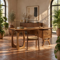 Wooden desk with an oval leg frame, a wavy top and a side pedestal in a bright home office with arched windows and plants