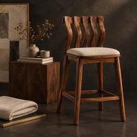 Corner detail of bar stool with a wavy slatted back and a padded seat beside wood, brass and linen samples