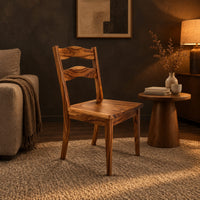Wooden chair with two wavy back slats and tapered legs in a dark living room at golden hour