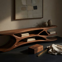 Corner detail of low TV console with carved web supports between shelves beside wood, brass and linen samples