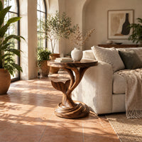 Side table with a carved whale tail on a spiral stem and coiled base in a bright living room with arched windows and plants