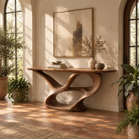 Console table with a winding ribbon base and a long tapered top in a bright entryway with arched windows and plants