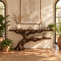 Console table with a leaning tree root base and one lower shelf in a bright entryway with arched windows and plants