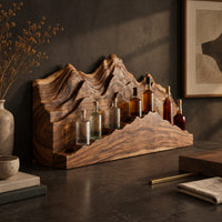 Corner detail of wine rack with layered carved mountain peaks and a ridge shaped ledge beside wood, brass and linen samples