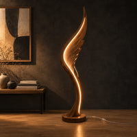 Wing shaped wooden floor lamp with a glowing edge line in a dark studio against a charcoal plaster wall