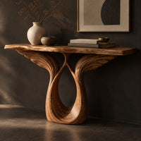 Corner detail of console table with feather carved wings rising from an open teardrop base beside wood, brass and linen samples
