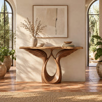 Console table with feather carved wings rising from an open teardrop base in a bright entryway with arched windows and plants