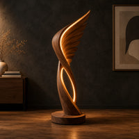 Winged floor lamp with layered feathers and a glowing oval loop in a dark studio against a charcoal plaster wall
