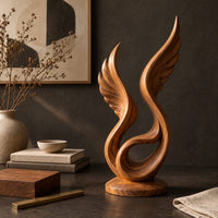 Corner detail of winged swirl sculpture with carved feather lines on a disc base beside wood, brass and linen samples