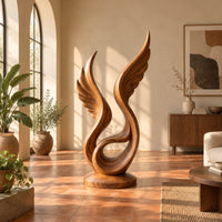 Winged swirl sculpture with carved feather lines on a disc base in a bright living room with arched windows and plants