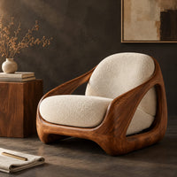 Corner detail of lounge chair with a carved wood shell frame and soft seat cushions beside wood, brass and linen samples