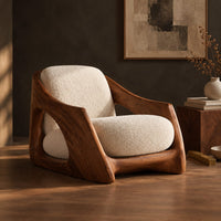 Corner detail of lounge chair with a carved wooden frame and soft cream cushions beside wood, brass and linen samples