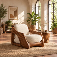 Lounge chair with a carved wooden frame and soft cream cushions in a bright living room with arched windows and plants