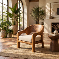 Wraparound lounge chair with arched cutout arms and an upholstered seat in a bright living room with arched windows and plants