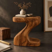 Corner detail of z shaped side table with a thick top and a flowing sculpted body beside wood, brass and linen samples