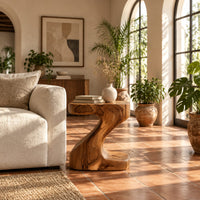 Z shaped side table with a thick top and a flowing sculpted body in a bright living room with arched windows and plants