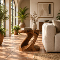 Z shaped side table with a carved diagonal opening and wide base in a bright living room with arched windows and plants