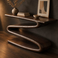 Corner detail of console table with a continuous zigzag ribbon base and a flat slab top beside wood, brass and linen samples