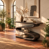 Console table with a continuous zigzag ribbon base and a flat slab top in a bright entryway with arched windows and plants
